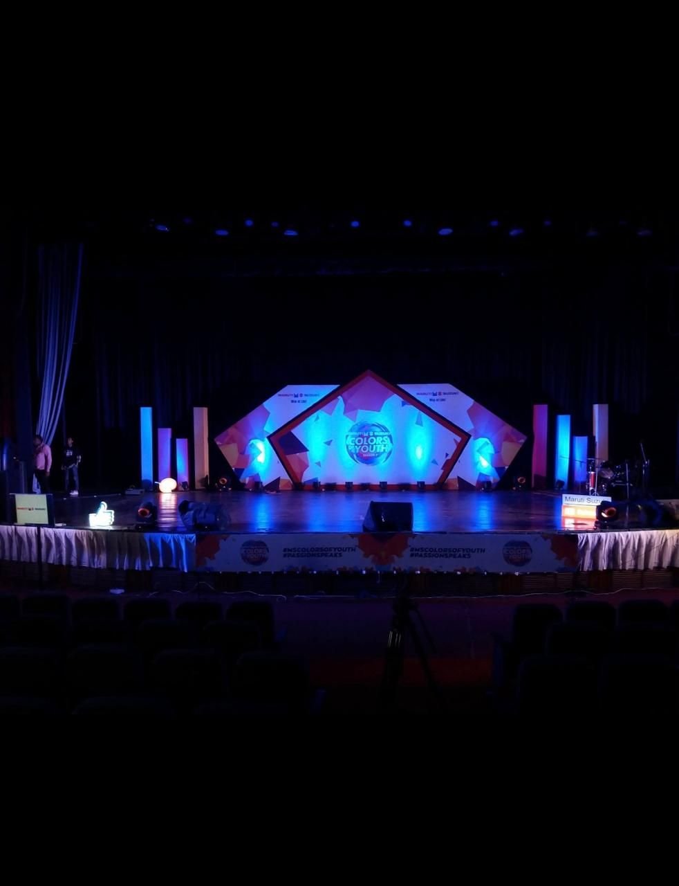 Auditorium stage lit in deep blue with a geometric set and LED screen ahead of an award night