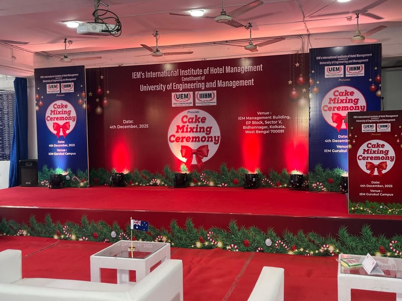 Festive ceremony stage with red carpet, uplighting and a branded backdrop at an institute