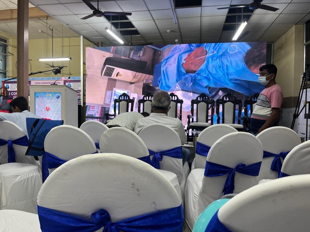 Conference hall with a large LED wall and rows of chairs dressed with blue sashes
