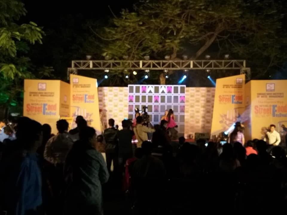 Audience in silhouette facing a brightly lit outdoor festival stage with truss rigging