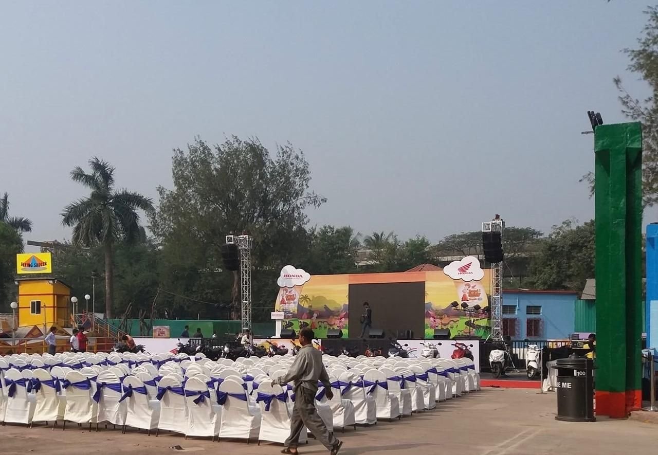 Open-ground event setup with rows of white chair covers and blue sashes facing a branded stage