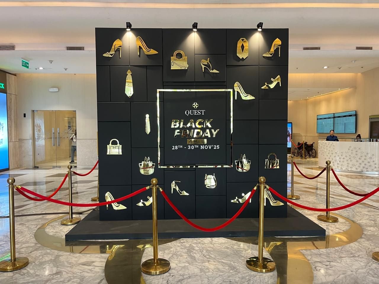 Black and gold retail campaign wall with lit product niches and stanchions in a mall atrium