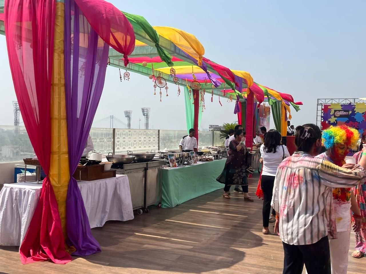 Rooftop festival with colourful fabric drapes over food counters on a sunny afternoon